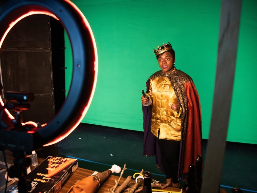 A student dressed in costume performs lines in front of a green screen